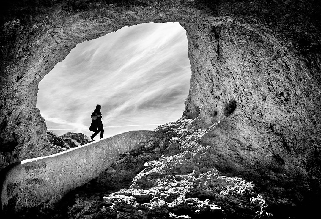 Una figura camina bajo una abertura excavada en la roca.